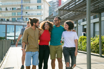 Joyous interracial friends enjoying walking outdoors. Mix raced group of people walking outside, hugging each other, talking and laughing. Multiethnic friendship concept