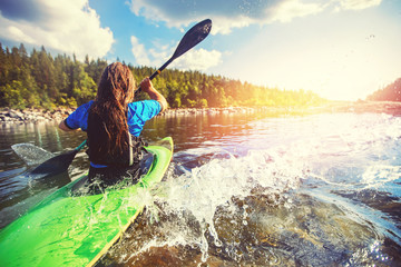 Young girl is kayaking with spray paddle splashes. Summer day, travel concept