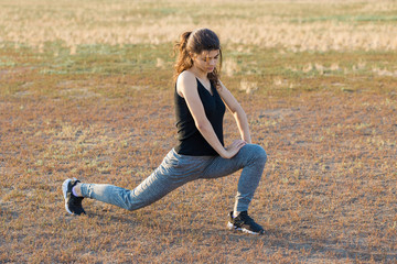 Slim sports girl performs leg stretching exercises on the nature.