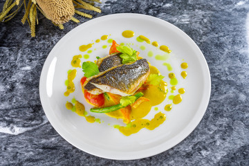 Top view cooked fillet sea bass with green sauce and vegetables on marble table. Grilld seabass...