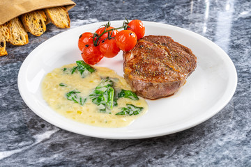 Close up view on restaurant served Medium Rare degree of Ribeye steak doneness with tomato and white sauce. Meat. Food for dinner. Flat lay food on marble table. American cuisine