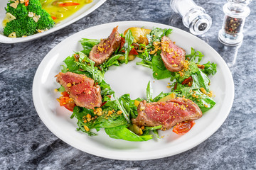 Close up view on Japanese cuisine styled salad Tataki with beaf (veal) spinach, arugula. Beef Tataki. Restaurant food for lunch. Flat lay food on marble table