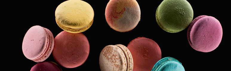 heap of delicious colorful French macaroons of different flavors isolated on black, panoramic shot