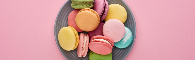 top view of multicolored delicious French macaroons on plate on pink background, panoramic shot