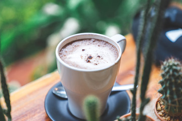 close up side view white mug of hot chocolate on wooden table with cactus