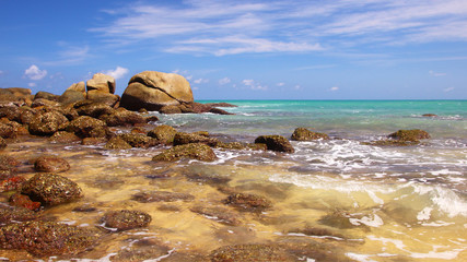 Boulders, the surf, and the blue sky over the sea, Karon sandy beach, Thailand