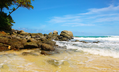 Boulders, the surf, and the blue sky over the sea, Karon sandy beach, Thailand