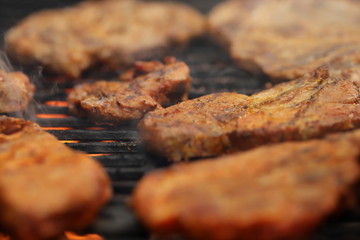 closeup on crispy grilled meat on smoking hot cast-iron grate with flames underneath- realistic food and barbecue party concept - foreground and background blanked out blurry