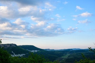 View of the gorge with growing green trees and white stone, from the top in the light of the setting sun, with clouds in the sky.