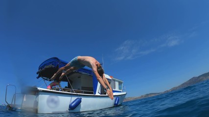Handsome young man jumping from a boat or yacht into the sea or ocean. Summer vacation with friends. Tourists have fun and dive. Slow motion.