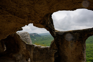 View of the mountain covered with a green carpet of trees and grass, through a window from a cave, on a bright sunny day, with clouds in the sky. Spring view of the Crimean mountains.