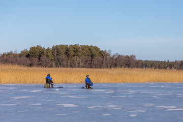 Ice fishing in Naantali, Finland. Sunny winter day with bright blue sky.