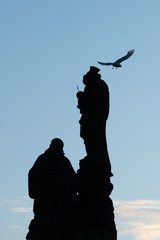 Silhouette of statue on Charles Bridge in Prague, with bird fly by. Medieval Gothic bridge, finished in the 15th century, crossing the Vltava River