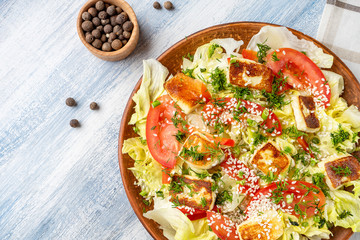 Top view on large plate with tasty salad: tomato, feta cheese, roasted meat chicken, asparagus and greens. Salad with copy space. Blue wooden background.