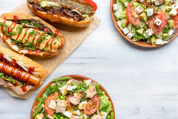 Top view food background with different dishes on plate. Flat lay with hot dog, salads and burger on light wooden background with copy space. Lunch time food. Frame