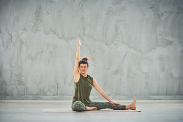 Beautiful Caucasian brunette in green sports wear sitting on the mat barefoot and doing yoga exercises. - Powered by Adobe