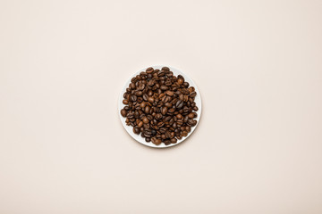 top view of coffee grains on white saucer on beige background