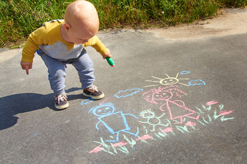 Fototapeta premium Little boy drawing with chalk on the asphalt, happy family: dad, mom and baby outdoors