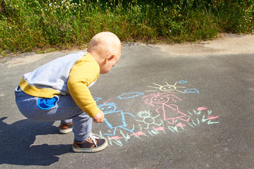 Naklejka premium Little boy drawing with chalk on the asphalt, happy family: dad, mom and baby outdoors