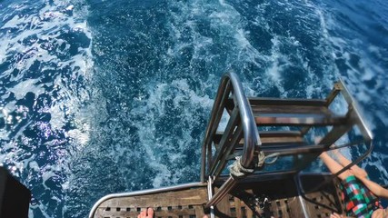 Handsome young man sits with his legs down from a boat or yacht in the sea or ocean. Plays with water, flying spray. Summer holidays with friends. Slow motion