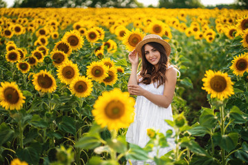 Fototapeta na wymiar european woman in a field of sunflowers, beautiful young european woman with dark hair in white long dress with hat on the nature