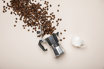 top view of metal coffee pot, cup and scattered fresh coffee beans on beige background