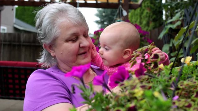 Happy and Beautiful Grandmother with short Silver Hair playing in the Garden with her 4 Month Old Cute Granddaughter. Happy Family Concept