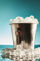 transparent ice cubes in metal bucket near water puddles on emerald and white background © LIGHTFIELD STUDIOS