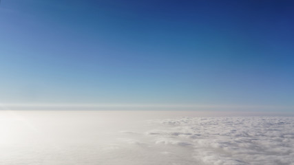 Beautiful white clouds and blue sky, viewed from the window of an airplane flying above the clouds.