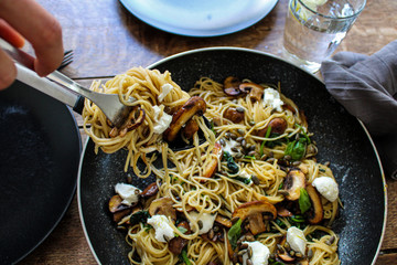 Mushroom and Spinach Pasta Topped with Goat Cheese and Pumpkin seeds. pasta being served. Top view. Food on a large pan on top of a wooden table. 