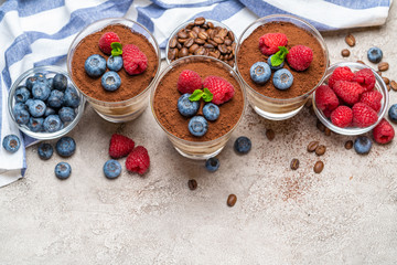 Classic tiramisu dessert with blueberries and raspberries in a glass and napkin on concrete background