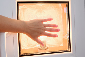 Light bulb in the window opening, hand in contact with the surface of the glass. Check the heat retention to install the Windows. Symbol of innovation. A spot of light on a blurred background.