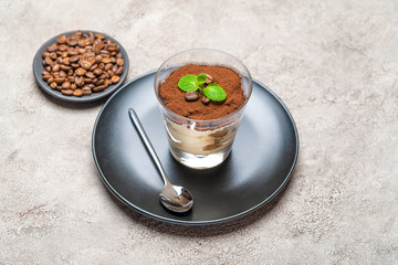 Classic tiramisu dessert in a glass cup on plate and coffee beans on concrete background