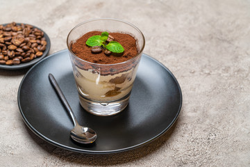 Classic tiramisu dessert in a glass cup on plate and coffee beans on concrete background