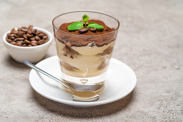 Classic tiramisu dessert in a glass cup on plate and coffee beans on concrete background