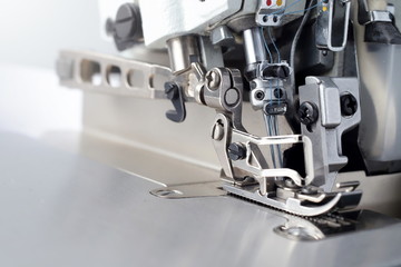 Mechanism of an industrial overlock sewing machine - closeup view on foot and needles with blurred...