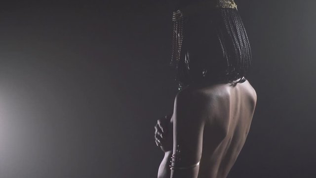 Cleopatra in low lighting, posing naked, view from the back, jewelry