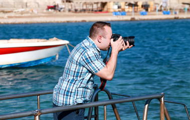 Professional photographer, tourist and traveler on sea pier is taking picture of environment, sea coast. Man on vacation in hotel resort on beach platform, he making landscape photography with camera.