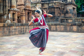 Indian classical dancer striking pose against the backdrop of  Mukteshvara Temple with sculptures in bhubaneswar, Odisha, India