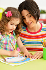 Close up portrait of little cute girl with mother drawing at the table at home