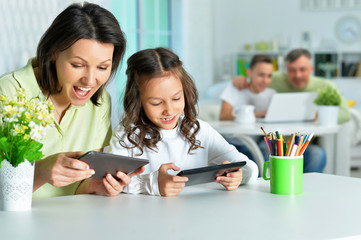 Portrait of smiling mother and daughter sitting at table and using digital tablets