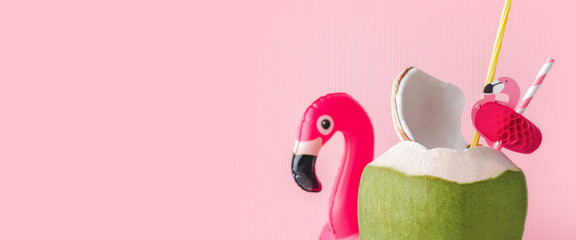 Fresh coconut on a pastel pink background with flamingo inflatable drink holder, summer vibes...