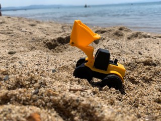 Excavator Bobcat Toy on the Sandy Beach with Sea Background in Sunny Weather