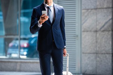 cropped view of man in suit using smartphone outside