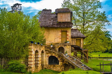 Lovely side view of the Mill with its garden, a rustic building with a thatched rooftop in the Queen's Hamlet surrounded by trees in the park of the Château de Versailles built for Marie Antoinette.