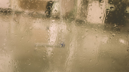 Rain Drops On Surface of wet Window Glass pane In Rainy Season. Abstract background. Natural Pattern of raindrops isolated from blurry city outdoor in a cloudy environment.