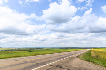 a long dirt road in rural North Dakota with a bright blue sky with clouds in the horizon
