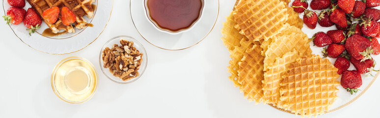 panoramic shot of waffles, strawberries, honey, nuts and tea on white