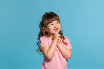 Beautiful little girl wearing in a pink t-shirt is posing against a blue studio background.