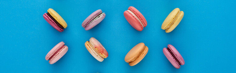 flat lay with sweet multicolored French macaroons on blue bright background, panoramic shot